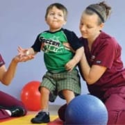 Physical therapist helping a child onto a platform