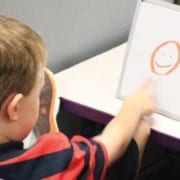 Child drawing a smiley face on a whiteboard