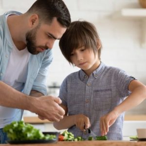 Father teaching son how to cut vegetables in the kitchen